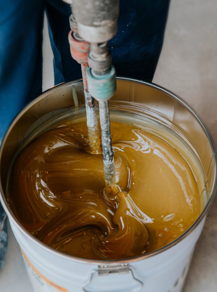Worker mixing yellow epoxy resin with the mixer in a tin bucket